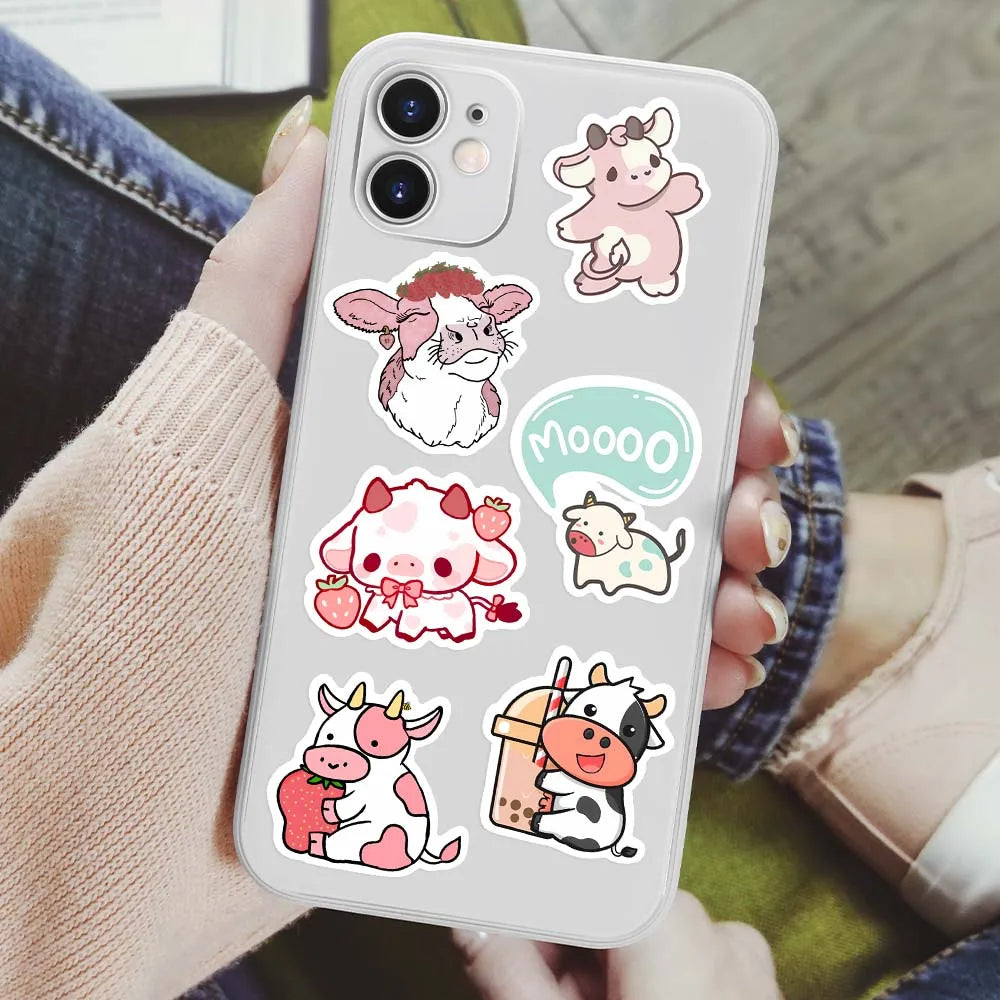 A smartphone displaying various cute pink cow cartoon decals and stickers on the back cover.