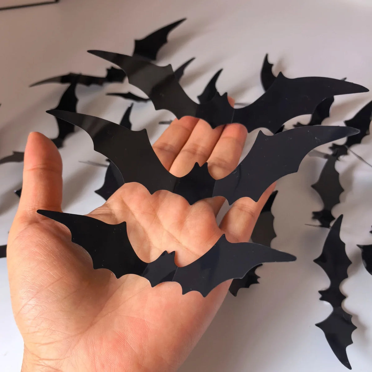 A hand holds black bat-shaped wall decals with glowing LED lights.