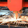 A close-up of a CNC machine cutting a piece of metal, creating sparks and bright light.