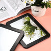 A black compact magnetic locker mirror is shown reflecting white flowers and a book.