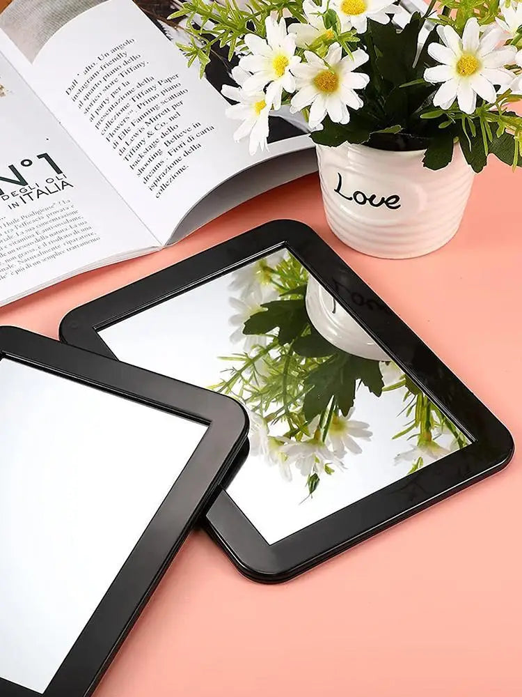 A black compact magnetic locker mirror is shown reflecting white flowers and a book.