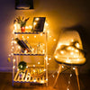 A wooden shelf displays LED star fairy lights illuminating various decorative items and a chair.