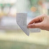 A hand is applying a self-adhesive window screen repair patch to a mesh screen, demonstrating a quick fix for holes or tears.