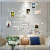 A gray wall decorated with white acrylic tree decals and framed photos, featuring a sofa and pillows.