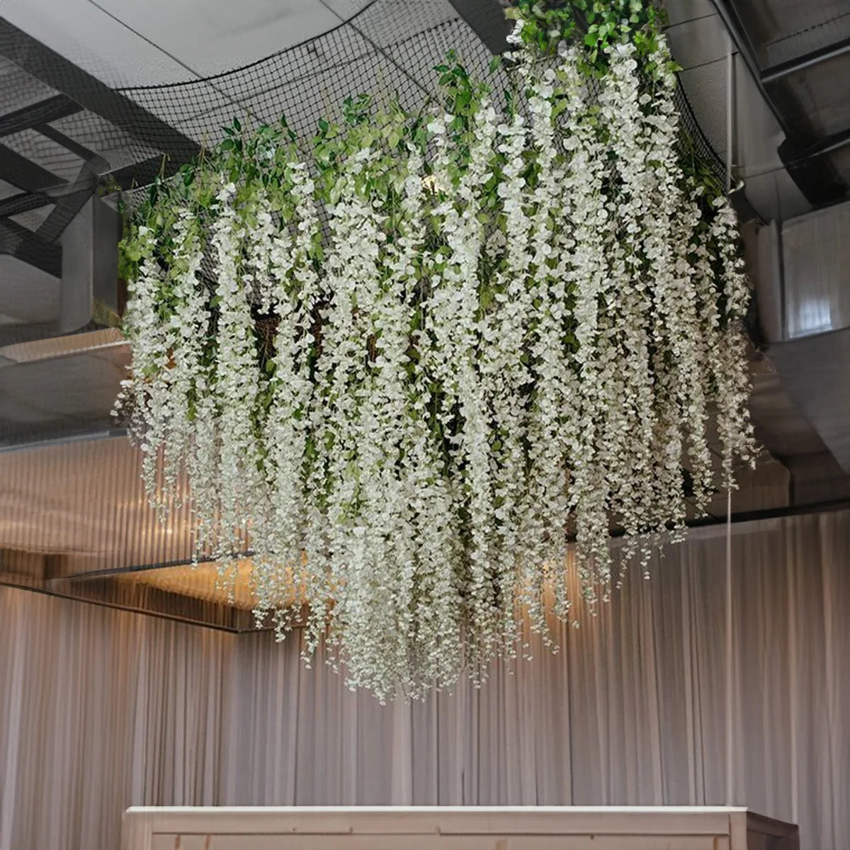 A dense cascade of white silk wisteria vine garland hanging from the ceiling in an indoor setting.