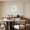 A round modern wall clock with gold 3D numerals hangs on a light beige wall above a wooden cabinet.