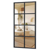 A tall rectangular mirror with a black frame reflecting a bright, modern interior with natural light and wood accents.