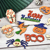 A collection of wooden Halloween ornaments including a skull, pumpkin, and spider, set against a light wooden background.