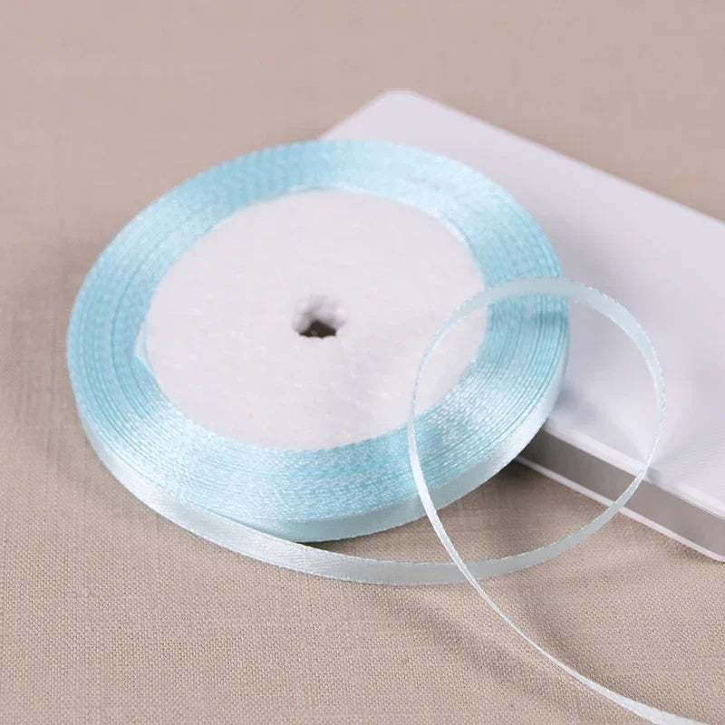 A roll of light blue satin ribbon on a white spool resting on a light beige surface.