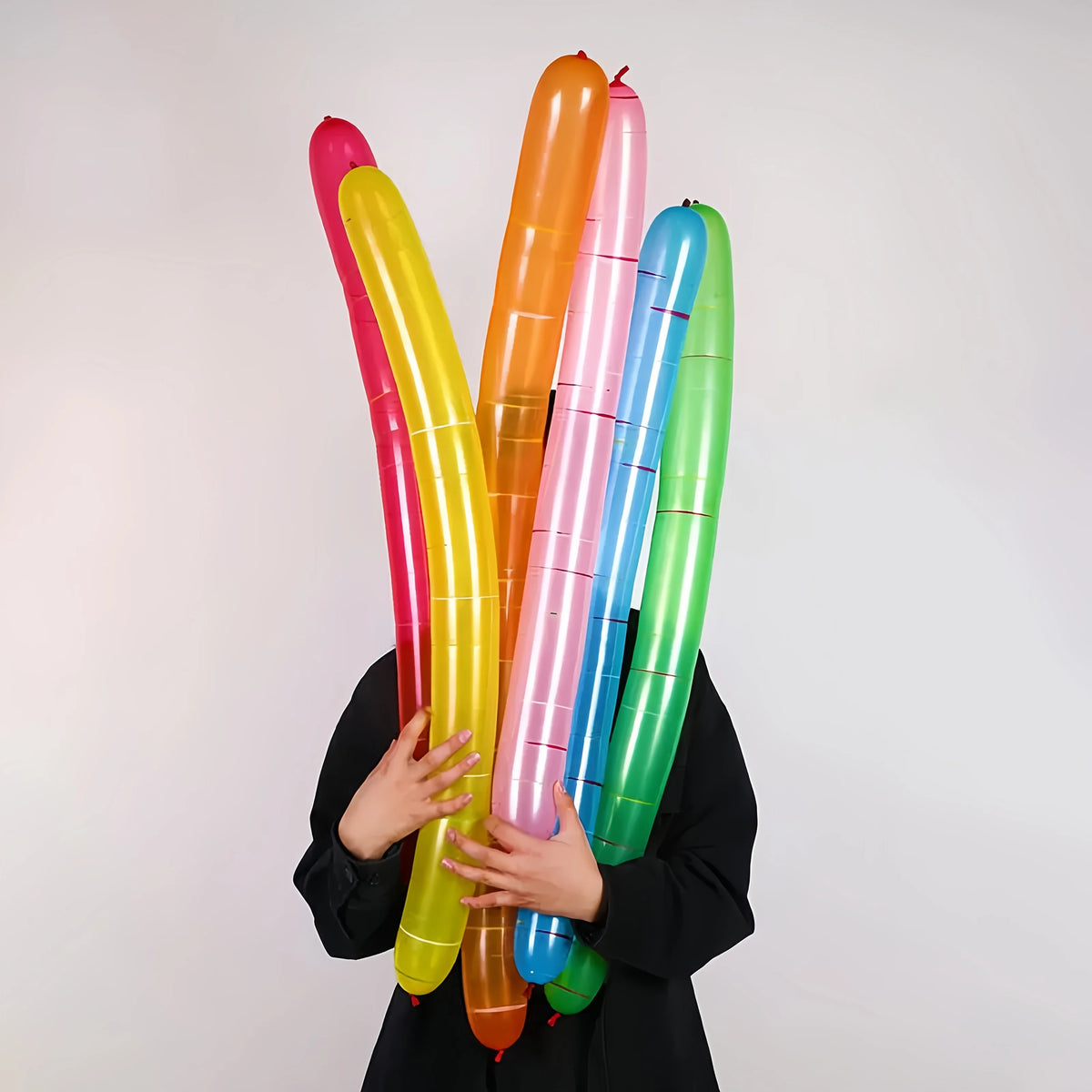 A hand holds a vertical arrangement of colorful balloon strips in shades of pink, yellow, orange, and green.