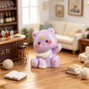 A purple resin cat keychain sitting on a wooden floor next to a book.