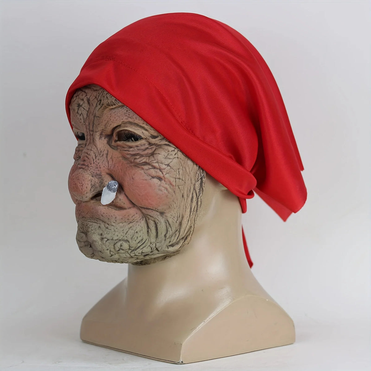 A realistic latex horror mask of an elderly woman with wrinkled skin wearing a bright red headscarf.