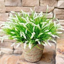 A potted artificial lavender plastic wreath with bright green foliage and white flowers sits on a stone surface.