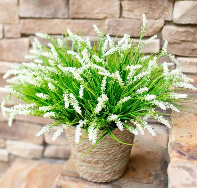A potted artificial lavender plastic wreath with bright green foliage and white flowers sits on a stone surface.