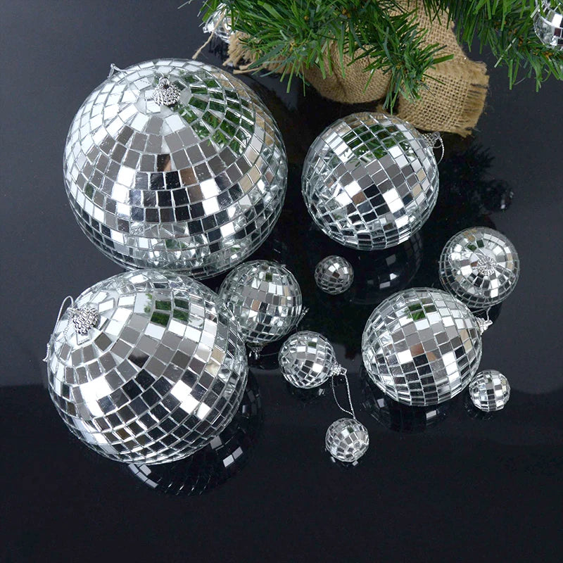 Silver disco mirror balls of various sizes scattered on a dark surface with pine greenery.