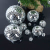 Silver mirror balls of various sizes scattered on a dark surface with pine greenery in the background