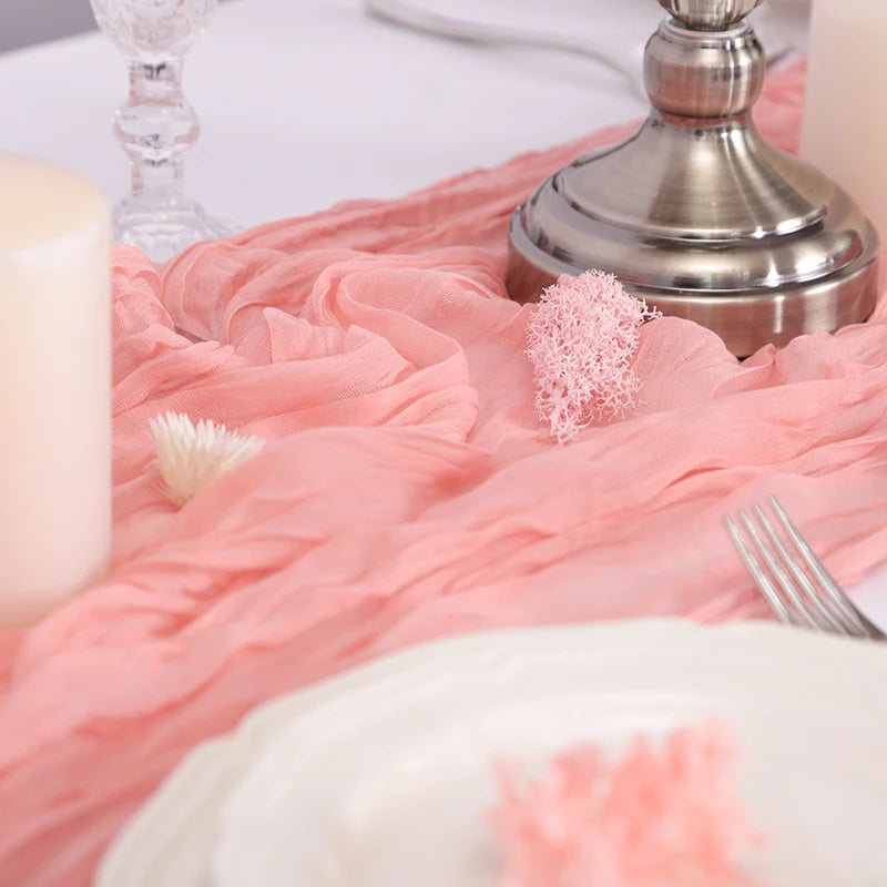 A pink gauzy table runner with a silver candlestick and white candle on a white surface.