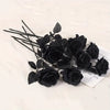 A cluster of artificial black roses and leaves arranged on a white surface.