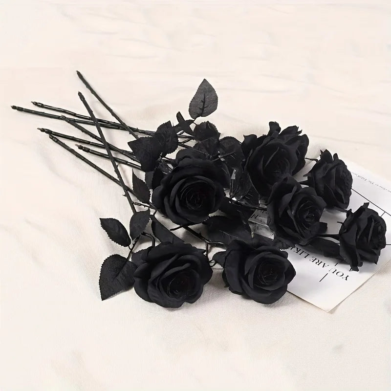 A cluster of artificial black roses and leaves arranged on a white surface.