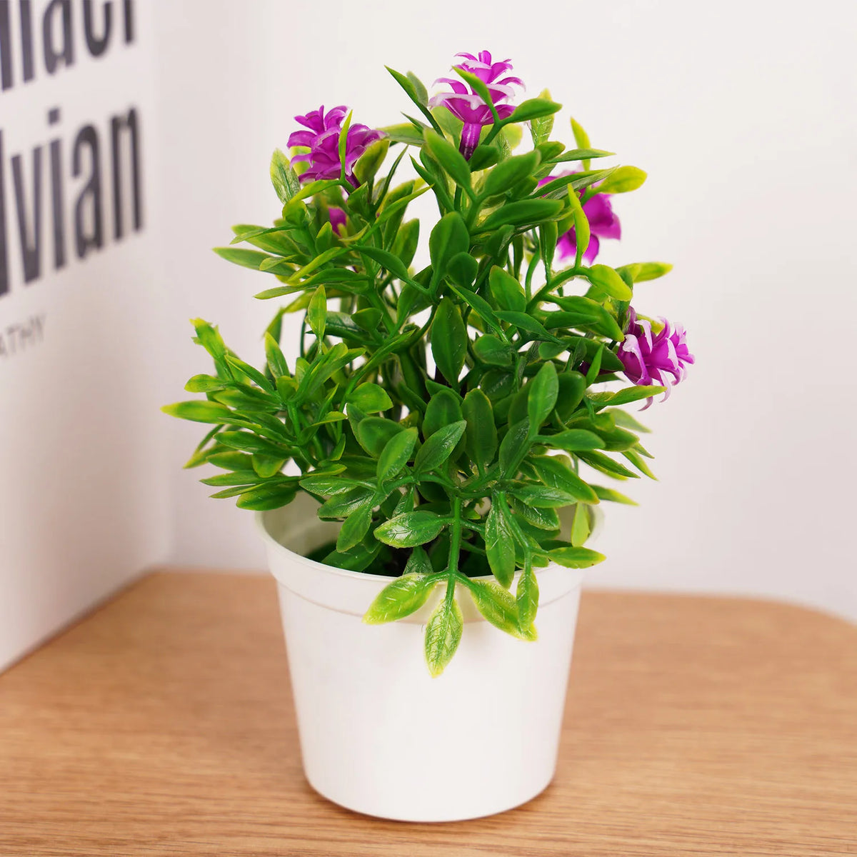 A potted artificial bonsai tree with vibrant purple flowers and green leaves on a wooden surface.