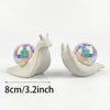A white snail sculpture with a iridescent disco ball shell resting on its back, measuring 8cm/3.2inch.