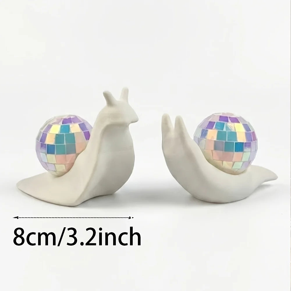 A white snail sculpture with a iridescent disco ball shell resting on its back, measuring 8cm/3.2inch.