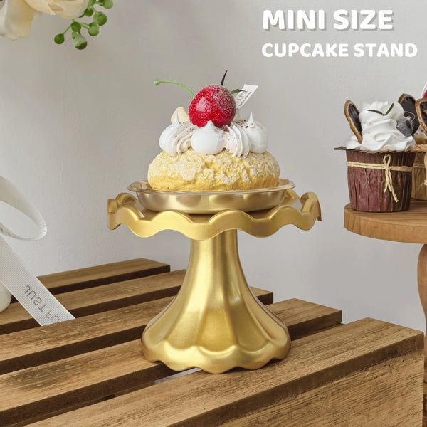 A golden mini cupcake stand displaying a single decorated cupcake with a red berry on a wooden surface.