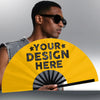 A man wearing sunglasses holds a yellow folding hand fan with the text Your Design Here on it.