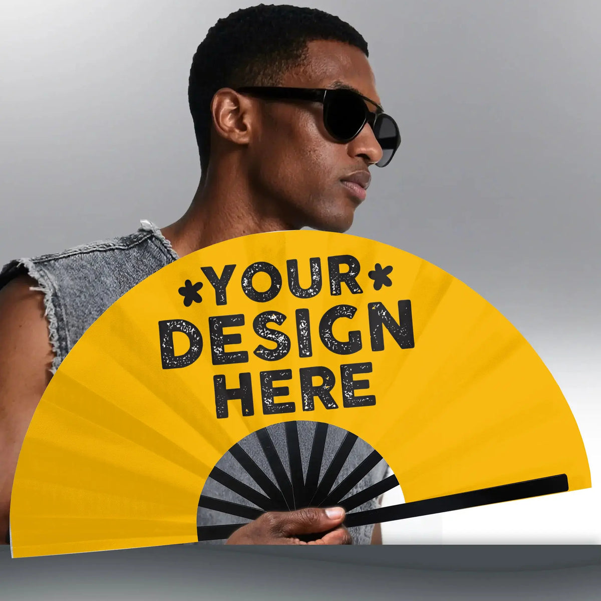 A man wearing sunglasses holds a yellow folding hand fan with the text Your Design Here on it.