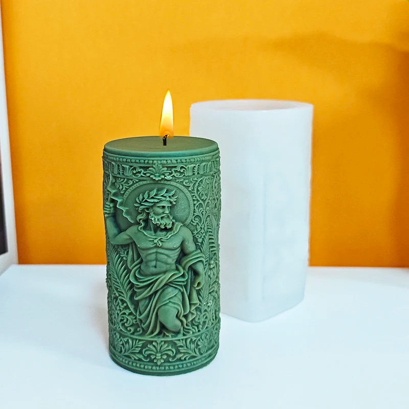 A green silicone candle mold shaped like a statue with a laurel wreath detail sits next to a white pillar candle on an orange