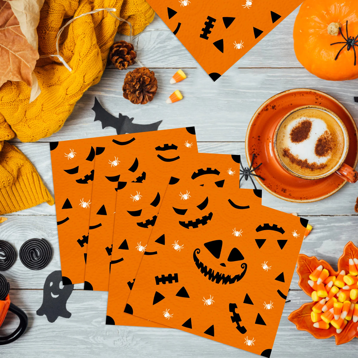 Orange paper napkins featuring black Halloween designs like skulls, spiders, and jack-o'-lanterns on a light wooden surface.