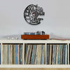 A black vintage vinyl record wall clock with the text The Kitchens The Heart of the Home mounted on a white wall.