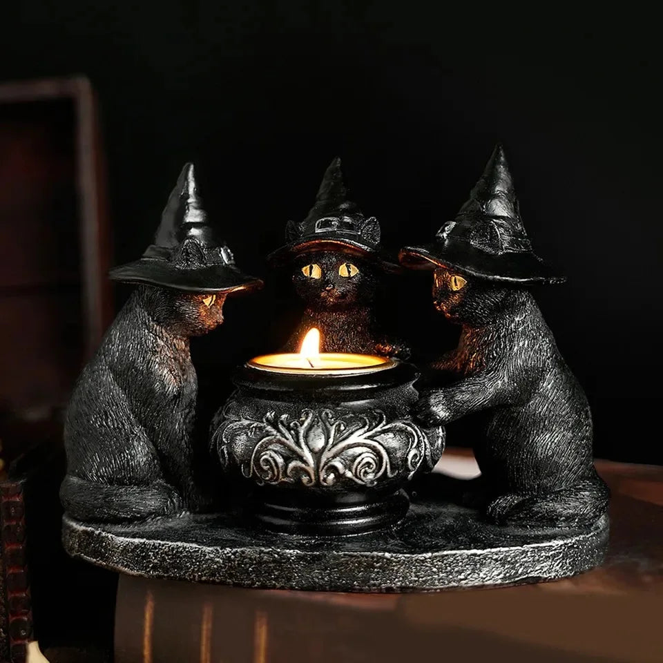 A dark metal figurine of three witch cats with pointed hats surrounding a lit candle on a round base.