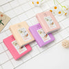 Pink and purple compact photo albums with instant film inserts arranged on a white grid surface.