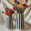 A tall ceramic vase with black and white vertical stripes holds a bouquet of colorful dried flowers.
