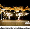 A glowing neon sign spelling Better Together is displayed on a dark surface with floral decorations.