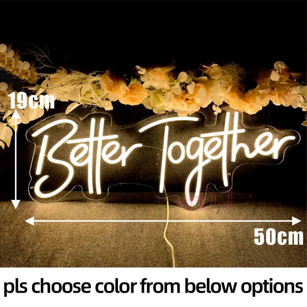 A glowing neon sign spelling Better Together is displayed on a dark surface with floral decorations.