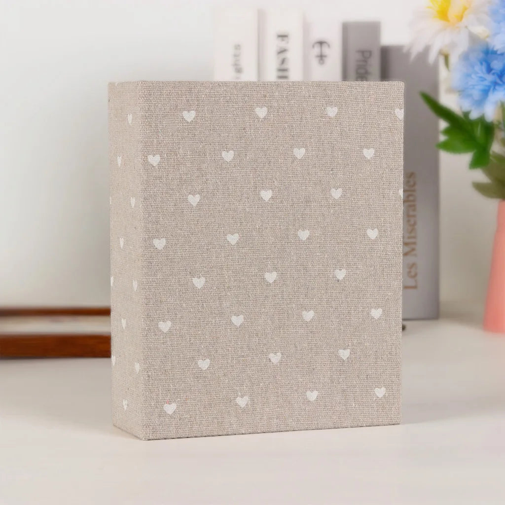 A square beige photo album with a textured cover featuring small white heart patterns, set against a white background.