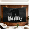 A black banner featuring the word BULLY in white stylized font displayed on a wooden wall.