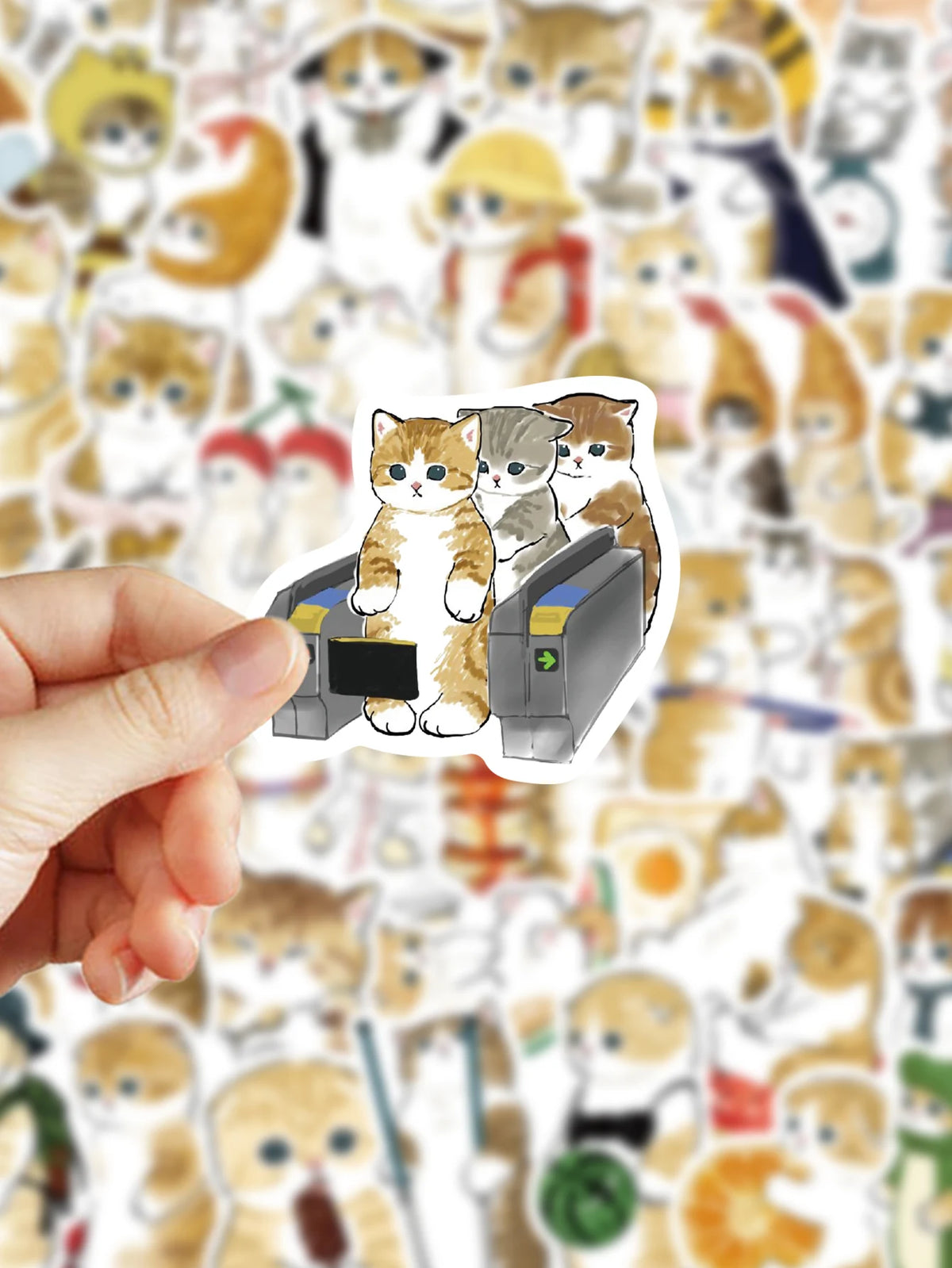 A hand holds a sticker featuring three cats sitting inside a dark gray box.