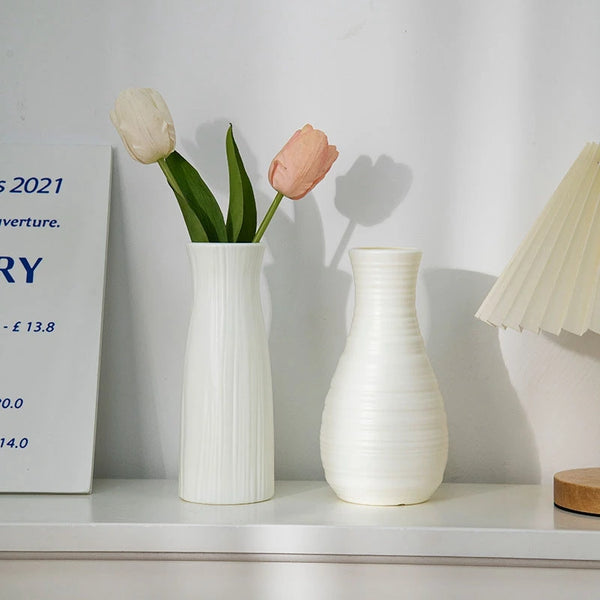 A white ceramic vase holds two pale pink tulips on a white shelf.