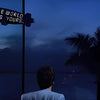 A silhouette of a person looking out over water with a sign that reads The world is yours on a dark sky background.
