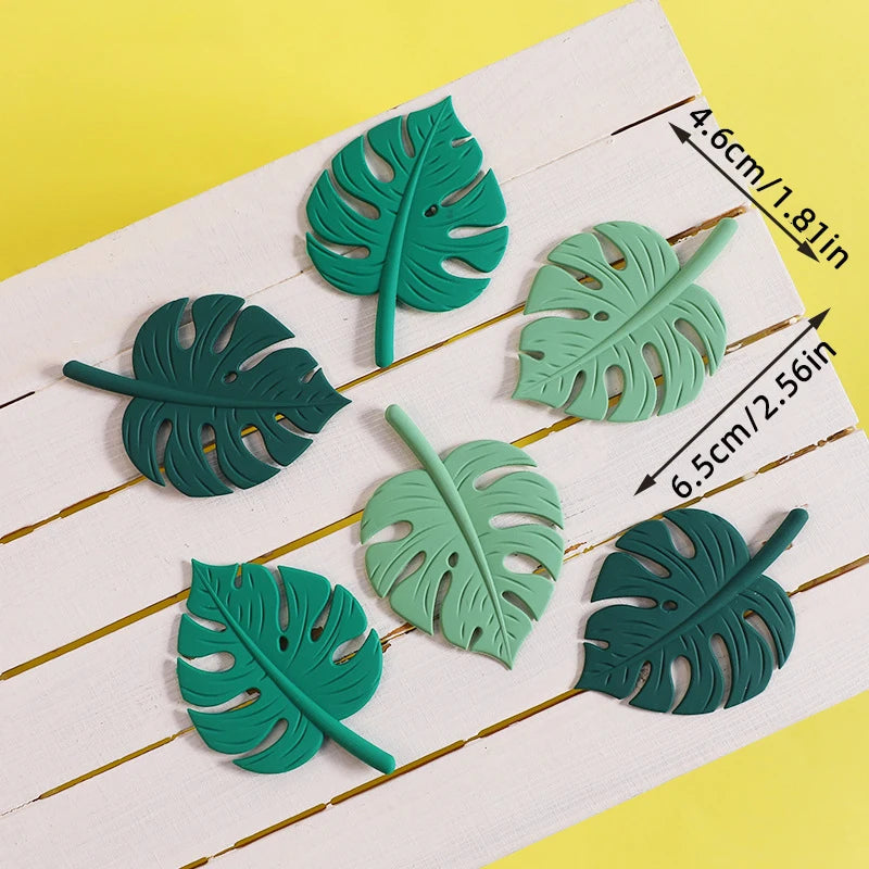 Un juego de seis toppers de hojas tropicales verdes sobre una tabla de madera blanca.