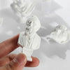 A white plaster bust miniature of a bearded man, likely a Greek deity, held in a hand against a bright background.