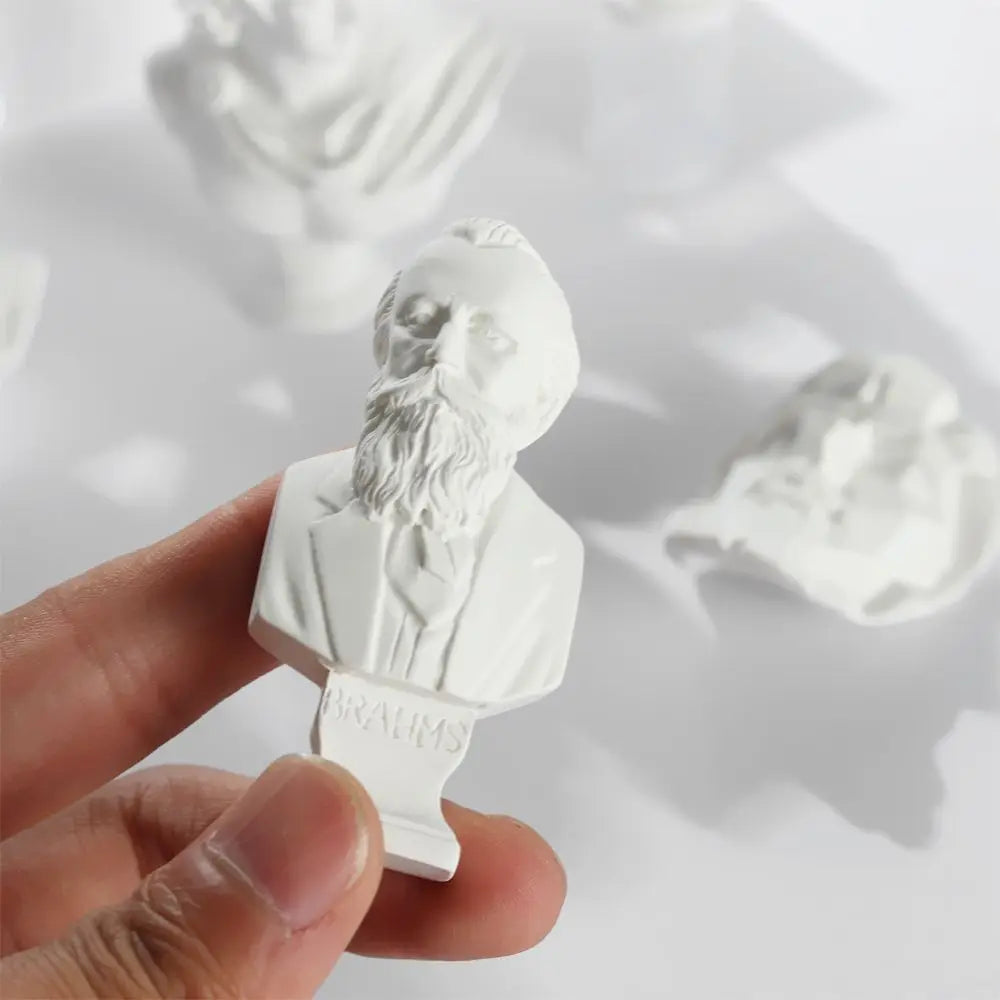A white plaster bust miniature of a bearded man, likely a Greek deity, held in a hand against a bright background.