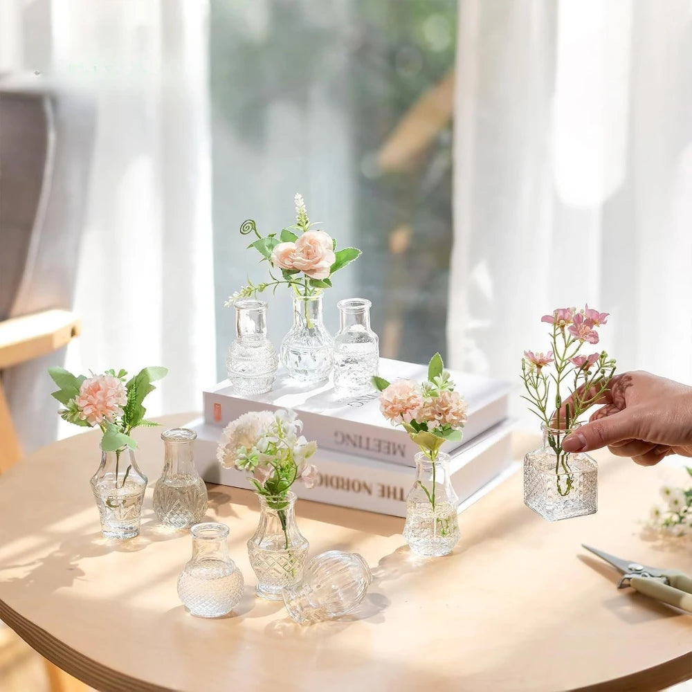 A collection of diamond faceted glass bud vases and small glass vessels arranged on a wooden table next to a book.