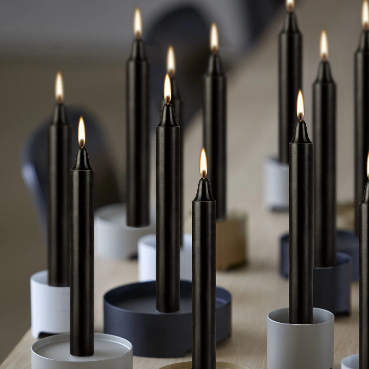 A collection of black taper candles in various holders, lit with flames, arranged on a wooden surface.