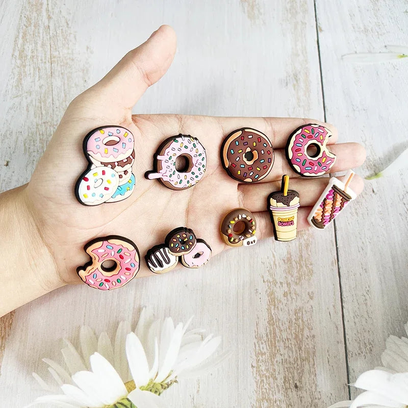 A hand holds various colorful doughnut-shaped charms for Crocs and slides on a light wooden surface.