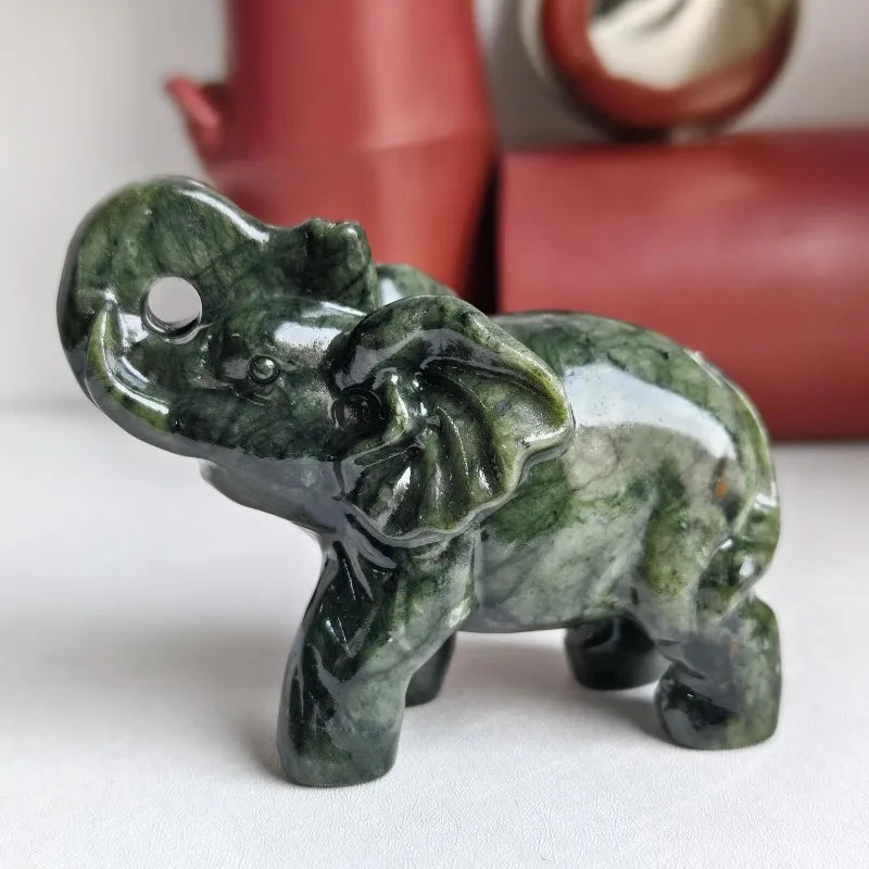 A small, carved statue of an elephant made from green jade resting on a white surface.