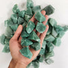 A hand holds a cluster of light green natural raw healing crystal stones for chakra balancing and home decor.